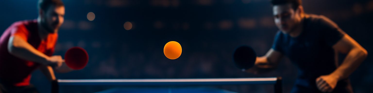Mesa de tenis de mesa azul iluminada con una pelota naranja en el aire sobre la red, imagen de esta comparativa de casas de apuestas de tenis de mesa